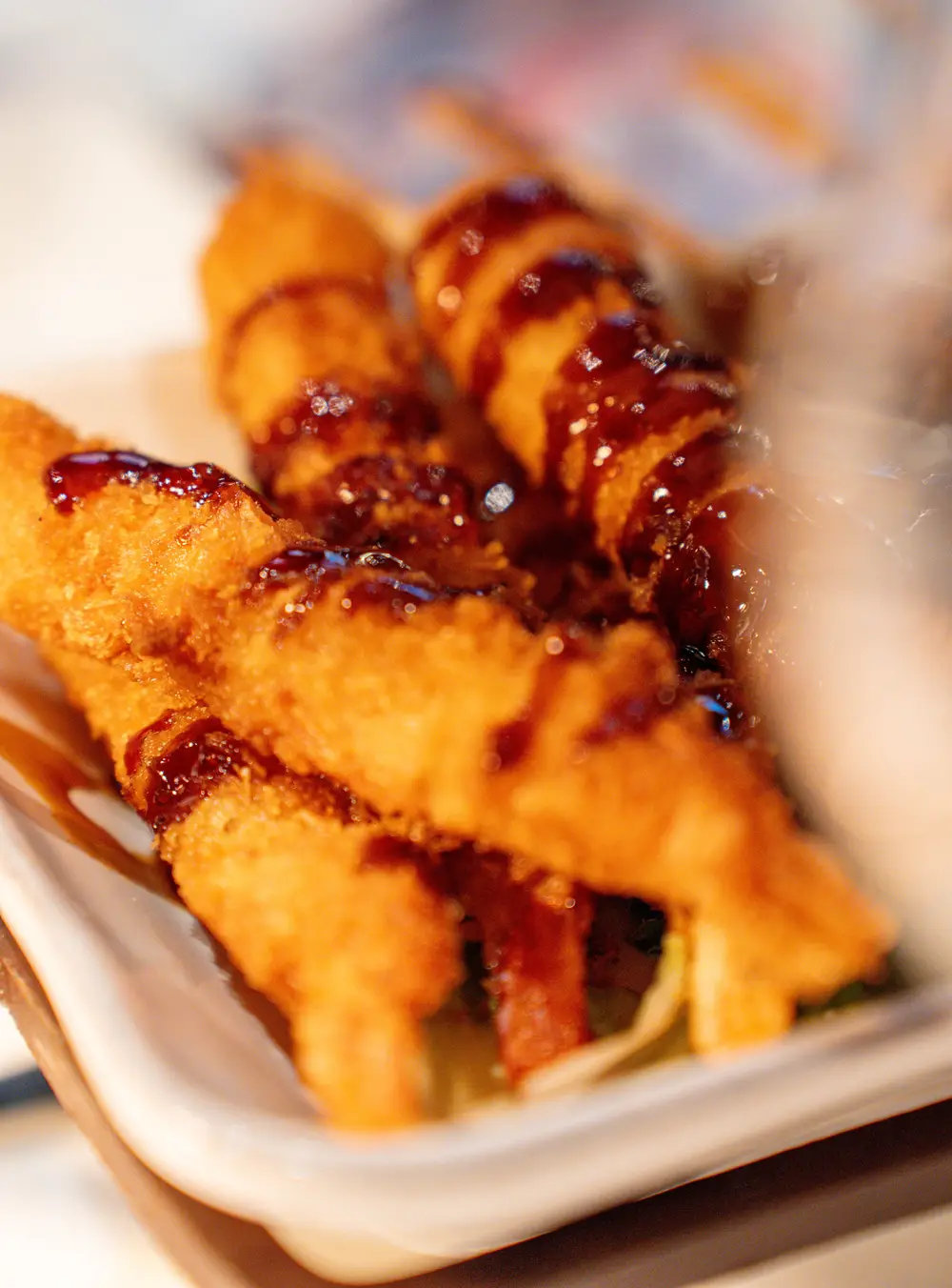 Frittierte Stücke mit dunkler Sauce auf einem weissen Teller, ganz nah fotografiert.