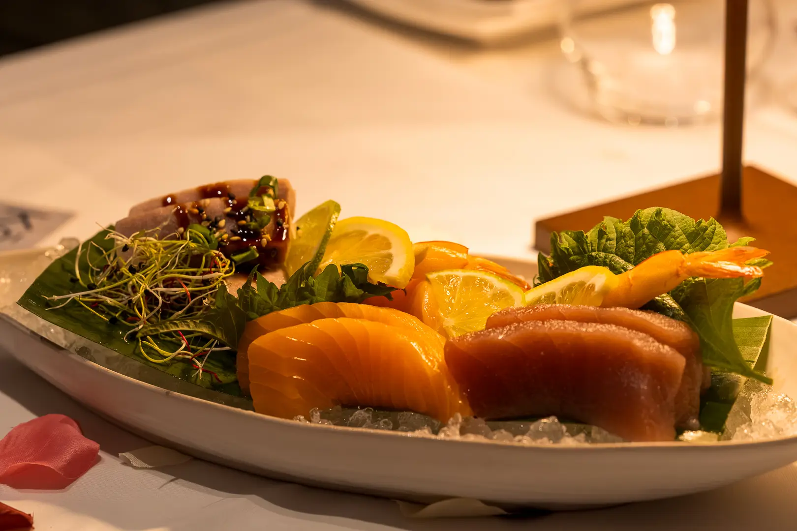 Eine lange Platte auf Eis mit rohem Fisch, Zitronenscheiben und Kräutern, im Hintergrund die Kerzen der Tafel.