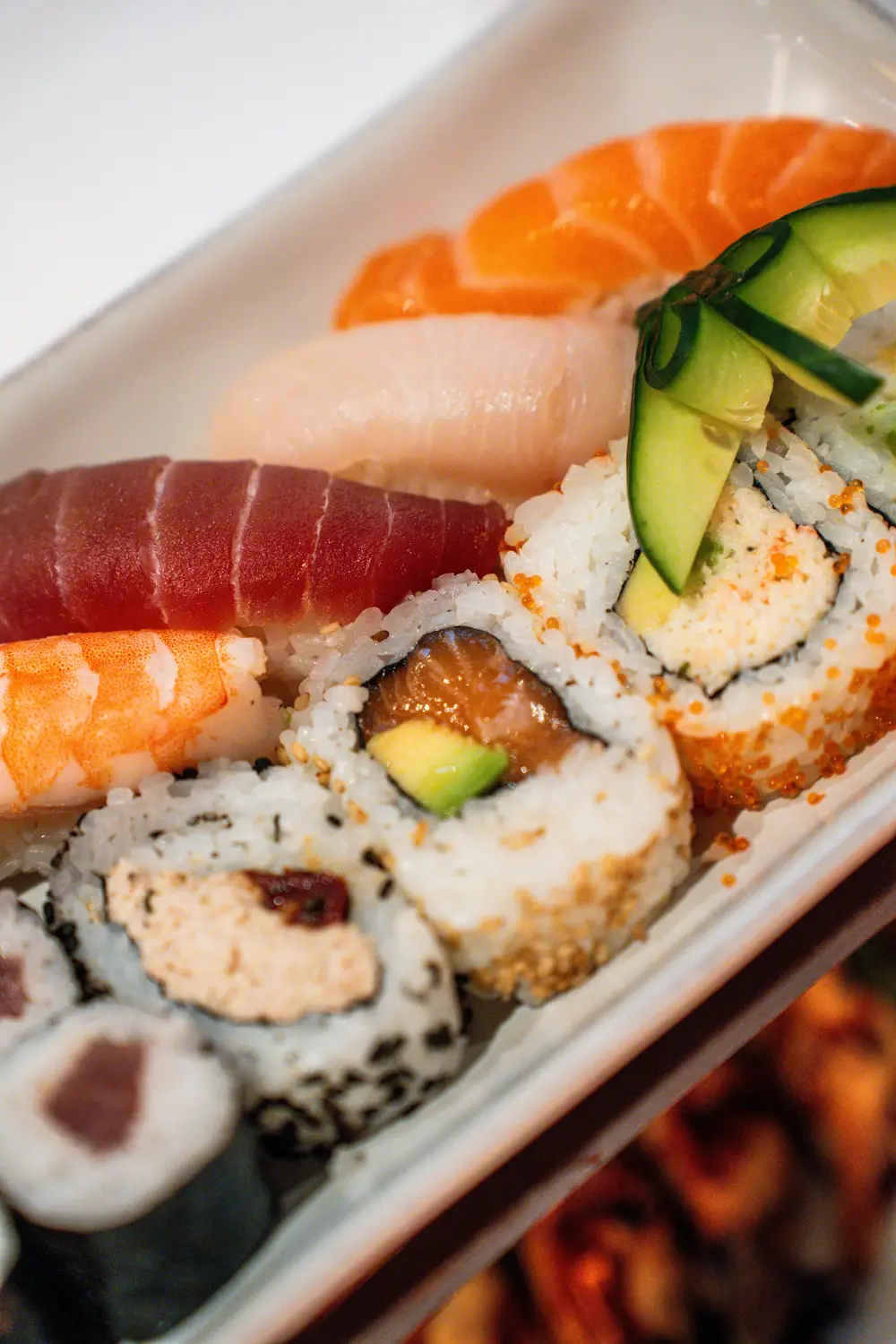 Eine weisse Platte mit Nigiri und Maki in mehreren Reihen, dahinter weitere Platten unscharf.