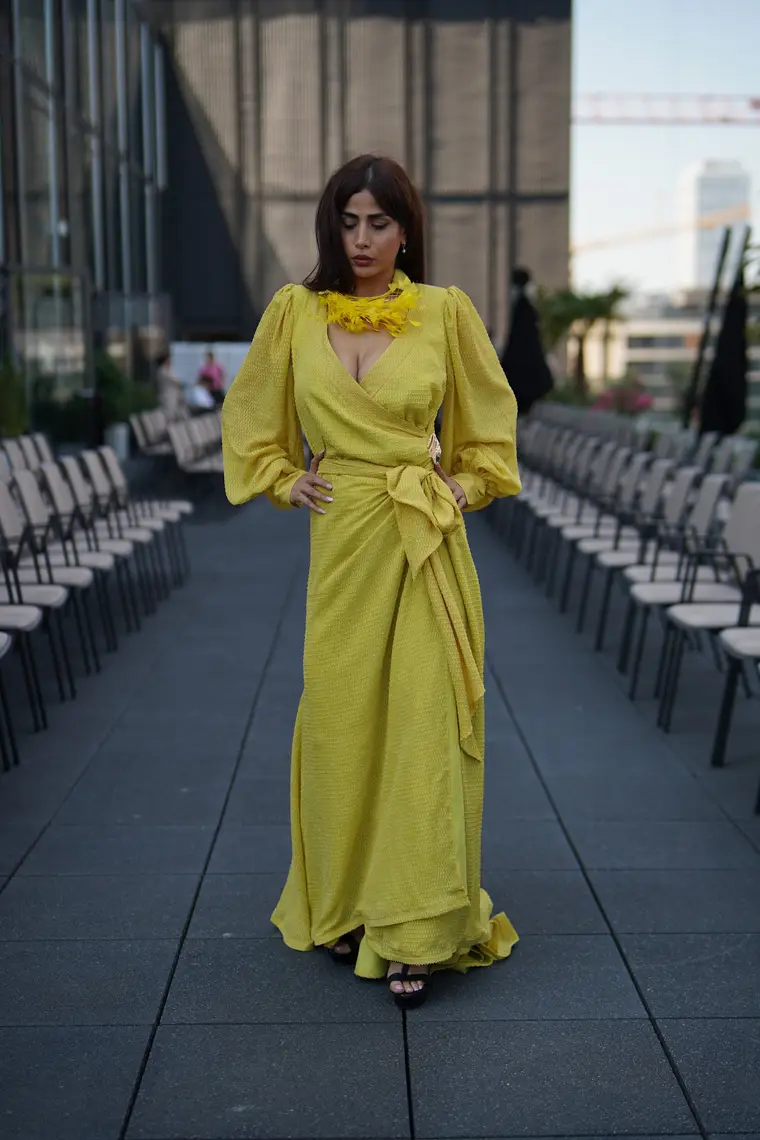 Model in einer langen gelben Robe mit floralem Halsstück auf einem Laufsteg.