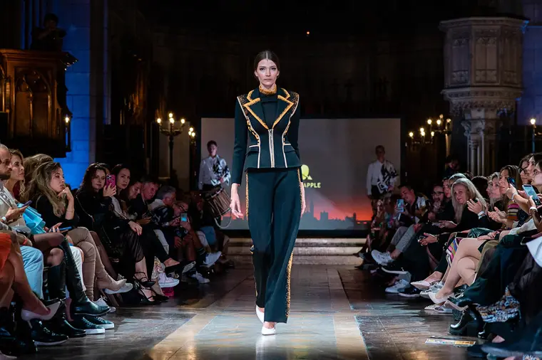 Model in einer dunklen, streng geschnittenen Jacke mit goldenen Details auf dem Laufsteg.