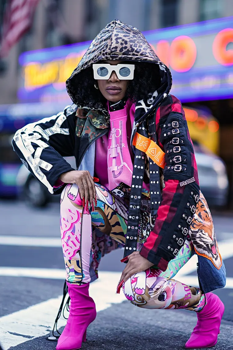 Model in einer Kapuze mit Leopardenmuster, weisser Sonnenbrille und einer bedruckten Jacke mit Schnallen, auf der Strasse.